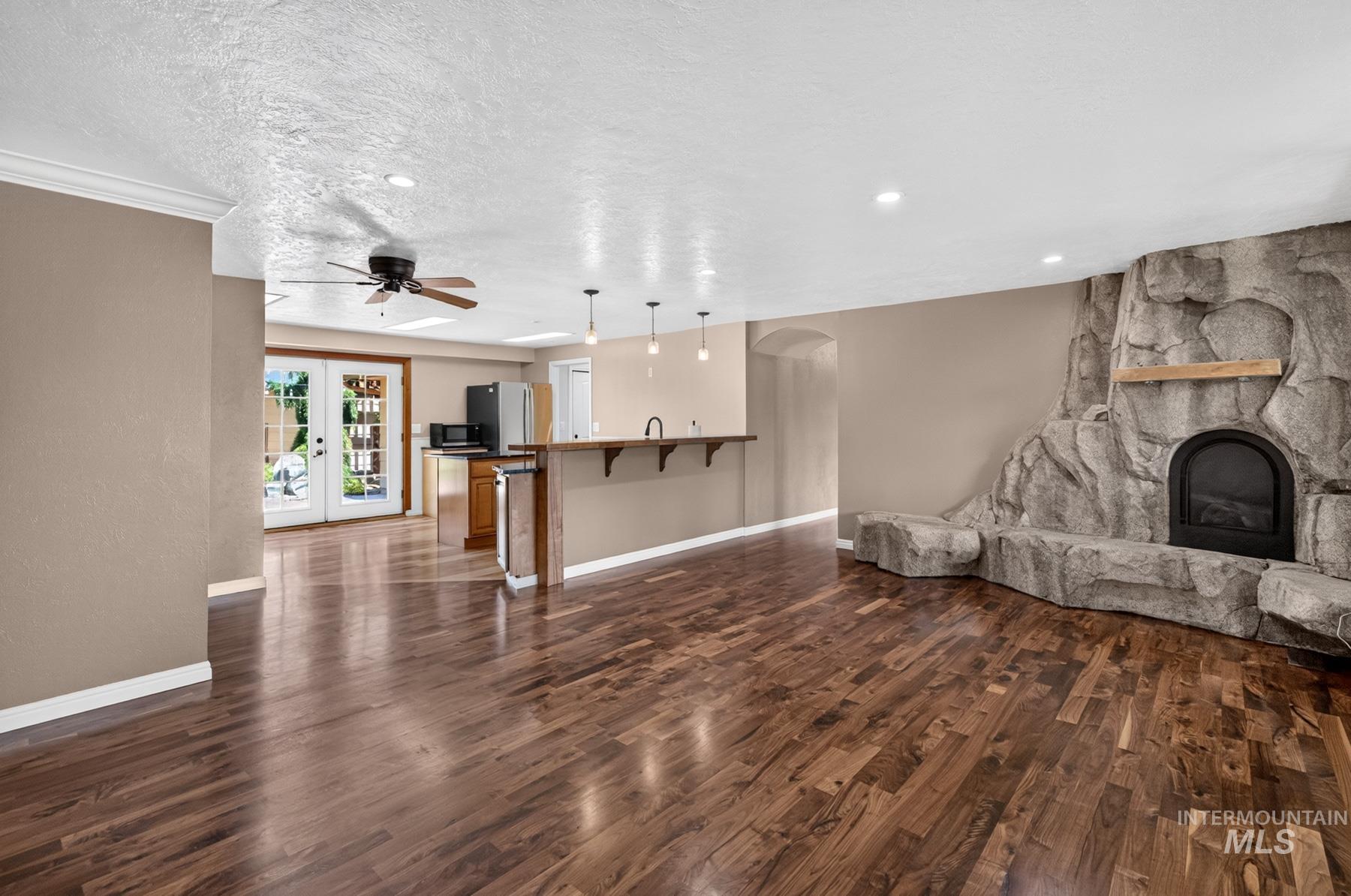 9622 Delaware Street Boise, ID 83709 - Photo 9 of 48 Spacious living area featuring rich wood-finish flooring, a prominent stone-clad fireplace with hearth seating, and a ceiling fan