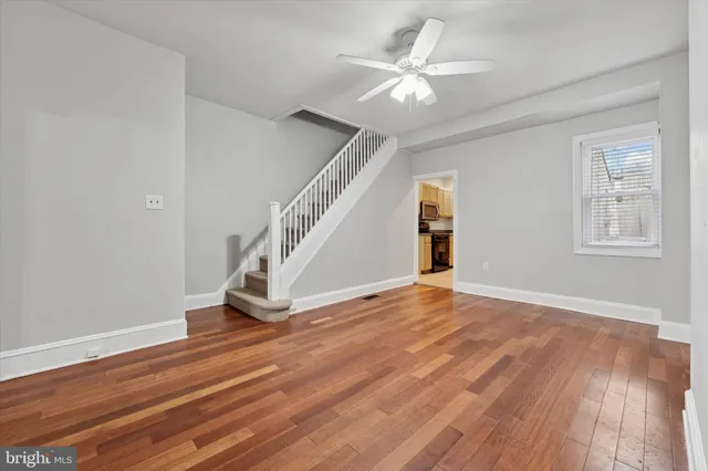 a view of an empty room with wooden floor and a ceiling fan