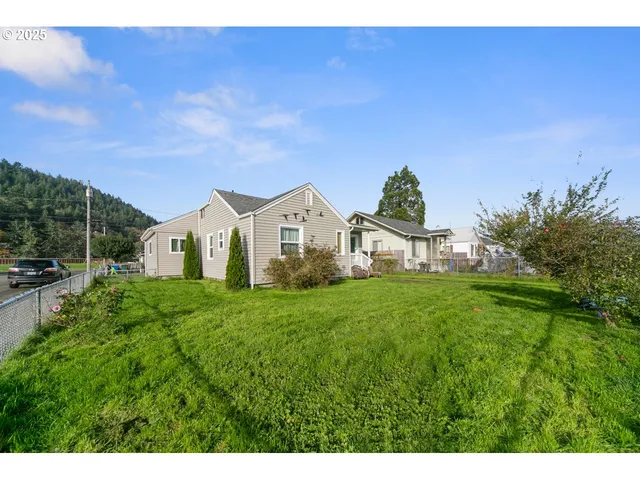 a view of a white house with a big yard plants and large trees