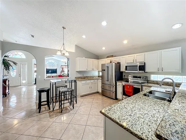 a kitchen with stainless steel appliances granite countertop a stove top oven a sink dishwasher and white cabinets with wooden floor