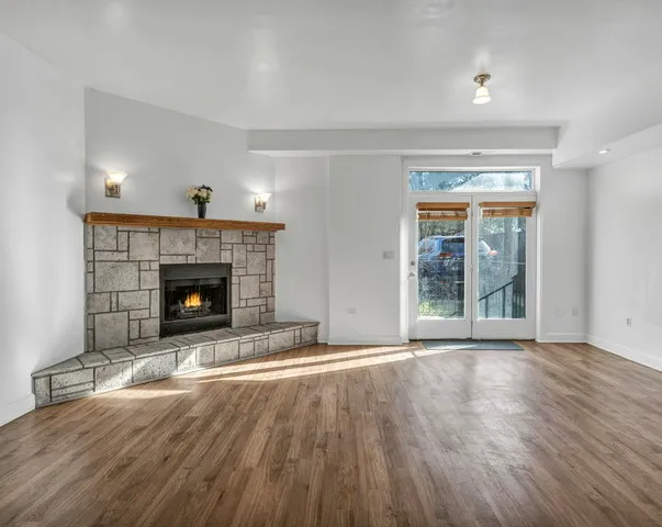 a view of an empty room with wooden floor fireplace and a window