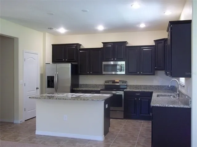 a kitchen with kitchen island granite countertop stainless steel appliances a stove a sink a refrigerator and cabinets