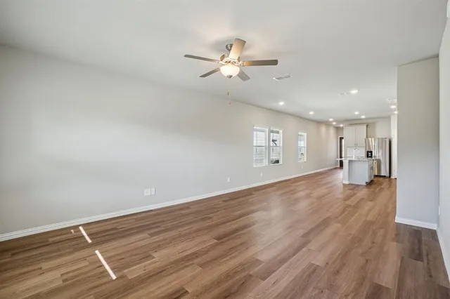 a view of an empty room with wooden floor and a ceiling fan