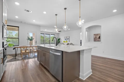 a kitchen with kitchen island granite countertop a stove a sink a dining table and chairs with wooden floor