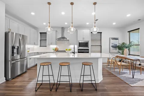a kitchen with stainless steel appliances kitchen island granite countertop a refrigerator a stove a island and chairs with wooden floor