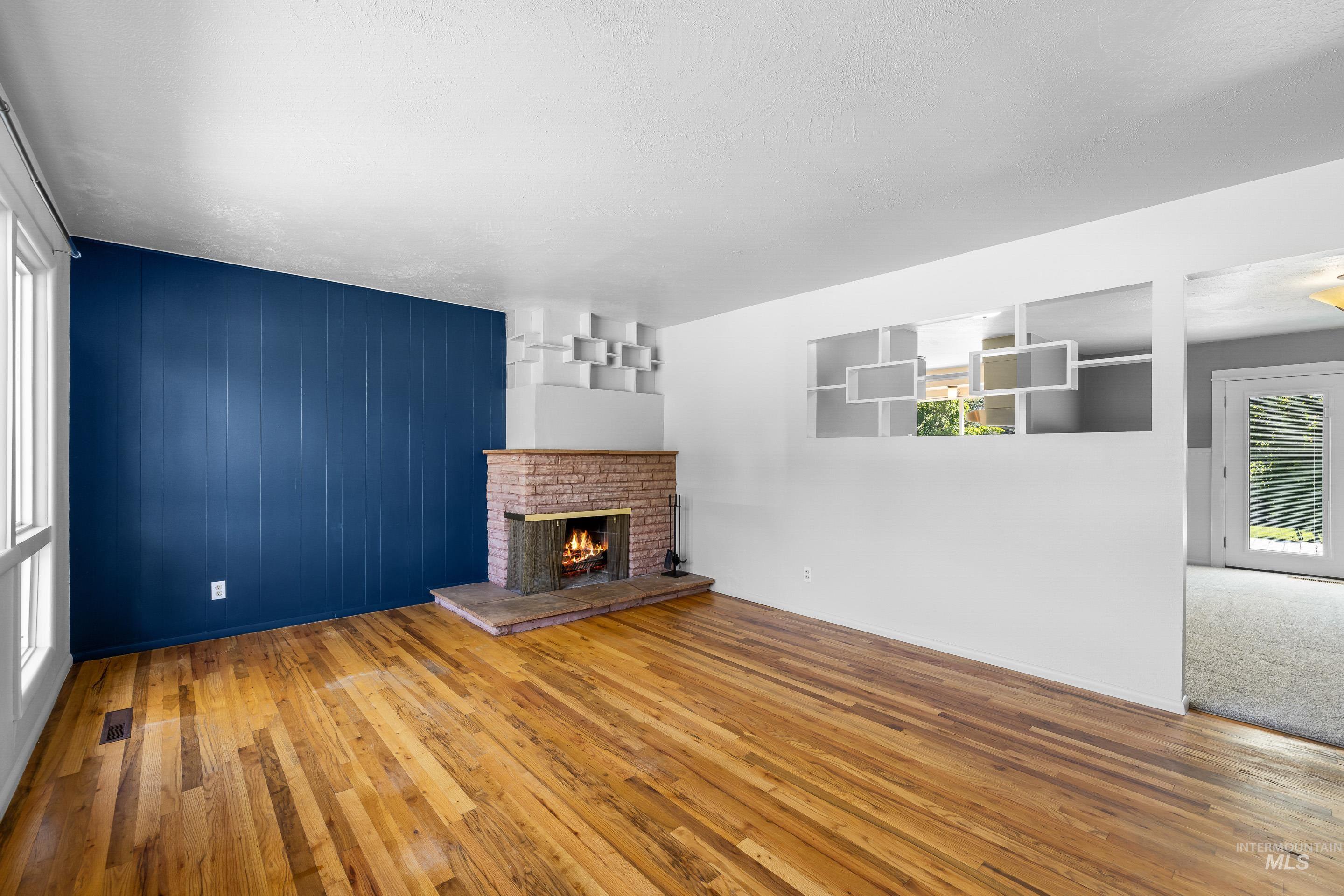 708 South Phillippi Street Boise, ID 83705 - Photo 4 of 25 Spacious room featuring wood-finish flooring, a brick fireplace with a stone hearth, and a blue paneled accent wall