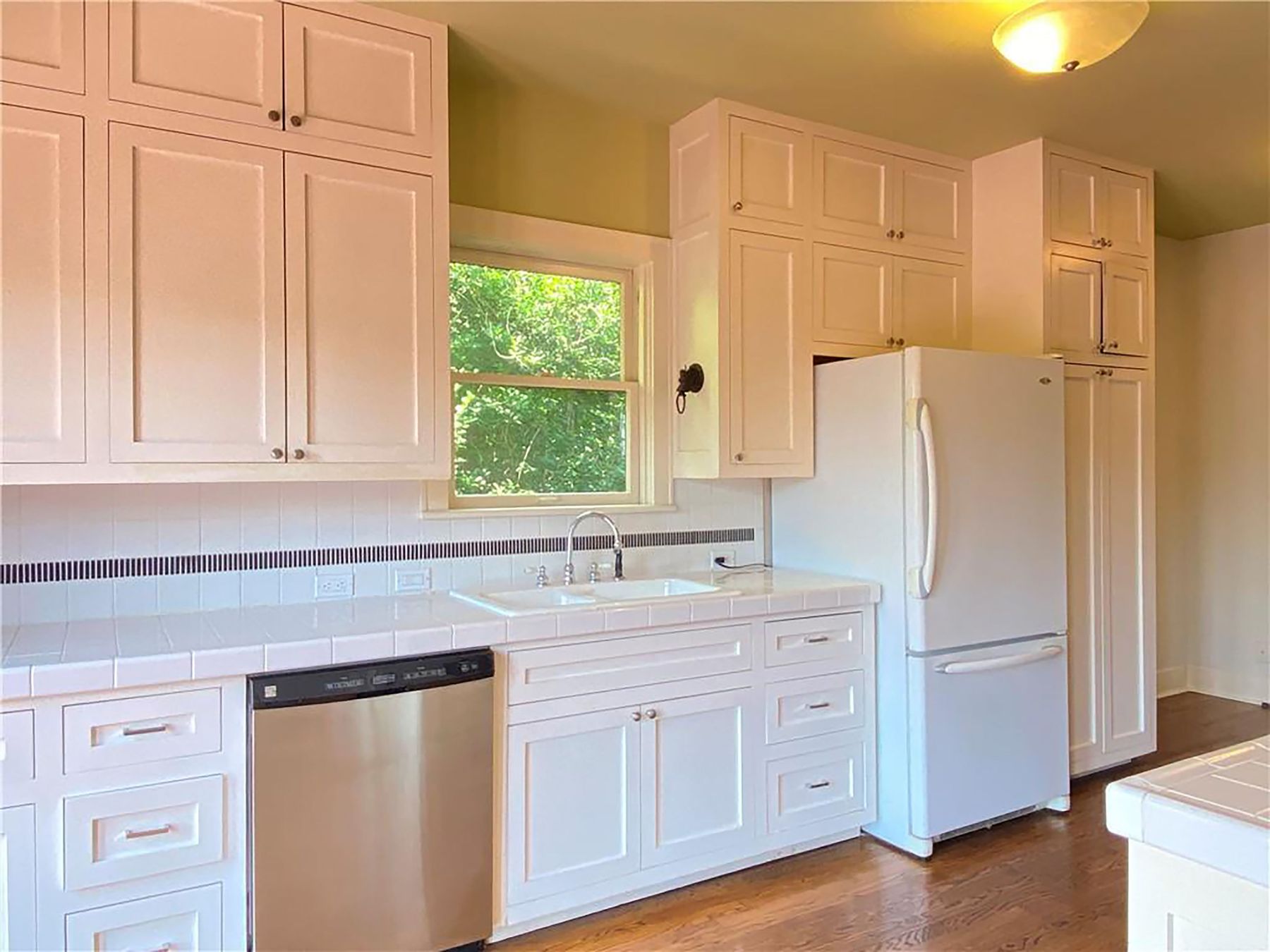 609 Texas Austin, TX 78705 - Photo 5 of 18 Kitchen featuring dishwasher, tile counters, freestanding refrigerator, and white cabinetry.