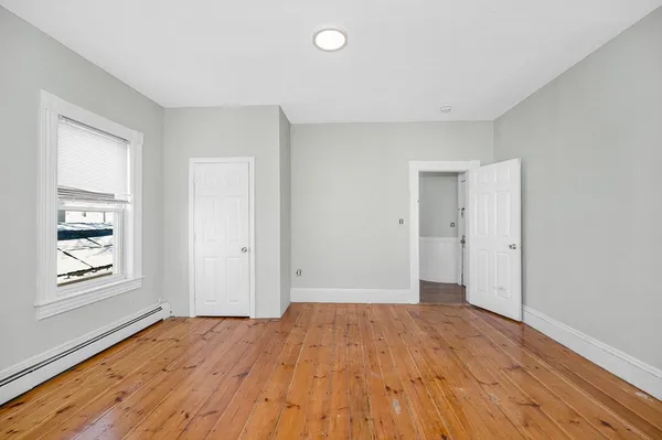 a view of an empty room with window and wooden floor