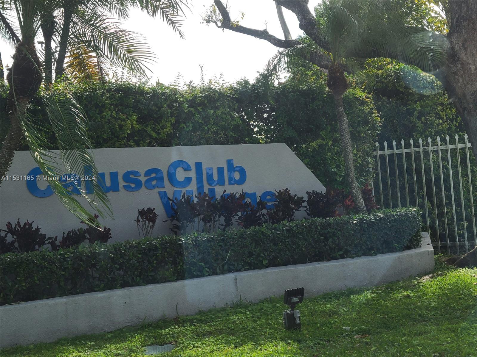 a view of a sign in a yard with potted plants and tree