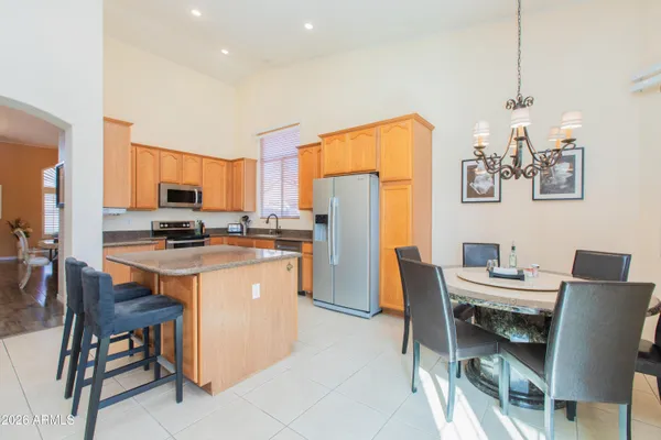 a kitchen with stainless steel appliances granite countertop a dining table chairs refrigerator and sink