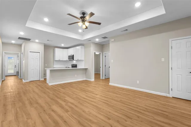 a view of an empty room and kitchen view with wooden floor