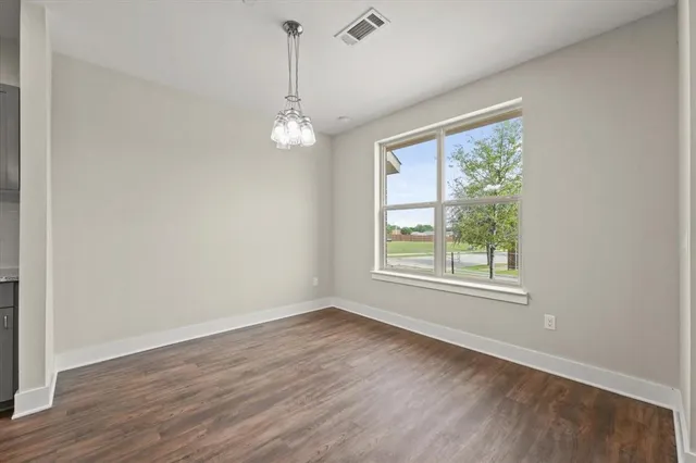 an empty room with wooden floor chandelier and windows