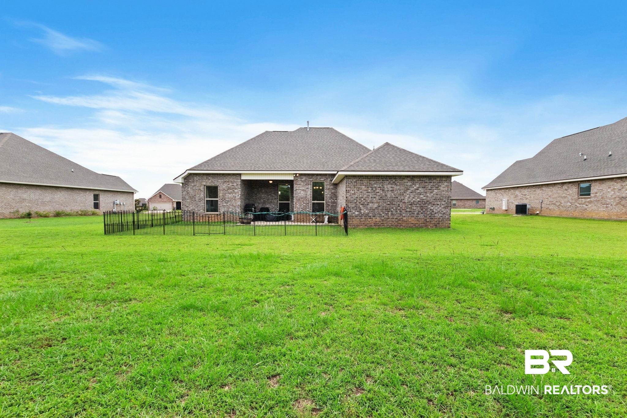 22244 Hibiscus Circle Foley, AL 36535 - Photo 5 of 51 Expansive green lawn with a partial black metal fence, a covered patio, and brick exterior