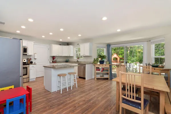 a kitchen with stainless steel appliances granite countertop a refrigerator a stove top oven a dining table and chairs with wooden floor