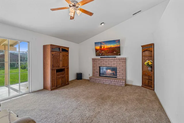 a view of a livingroom with a fireplace a ceiling fan and windows