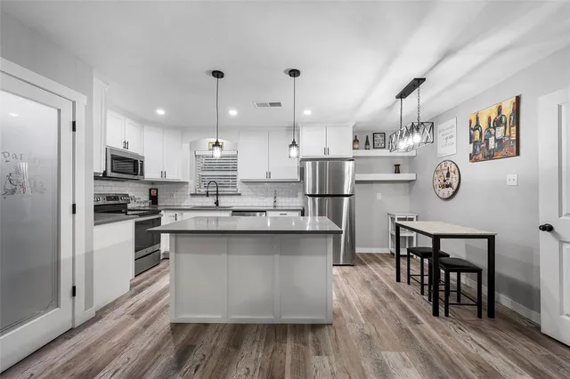 a large kitchen with a center island wooden floor stainless steel appliances and cabinets