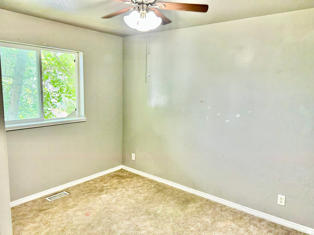 672 West 720 South Logan, UT 84321 - Photo 13 of 15 Room featuring a window with a green tree backdrop, a ceiling fan with light fixture, wall-to-wall carpeting, and white baseboards