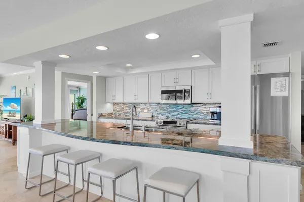 a kitchen with stainless steel appliances granite countertop a stove a sink a refrigerator and white cabinets with wooden floor