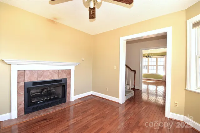 a view of an empty room with wooden floor fireplace and a window