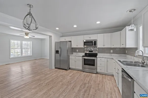 a kitchen with stainless steel appliances granite countertop a refrigerator a sink dishwasher a stove and white countertops with wooden floor