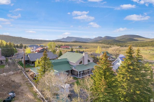 48 South Sage Road Pine Valley, UT 84781 - Photo 6 of 61 Property featuring a green metal roof, a covered wrap-around porch, multiple mature evergreen trees, and a mountain backdrop