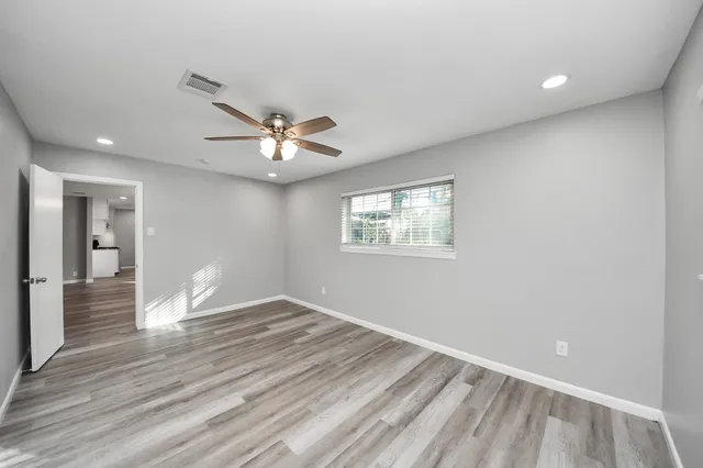 a view of an empty room with wooden floor and a ceiling fan