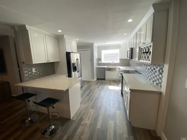 a kitchen with stainless steel appliances granite countertop a refrigerator a stove top oven a dining table and chairs with wooden floor