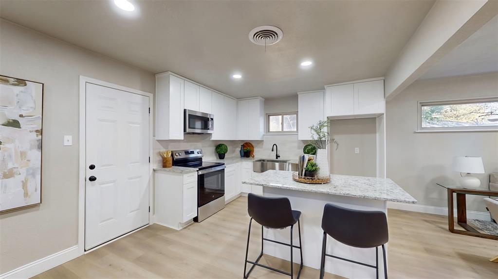 5009 Roxie Street Haltom City, TX 76117 - Photo 31 of 39 a kitchen with a refrigerator a stove a sink and white cabinets with wooden floor