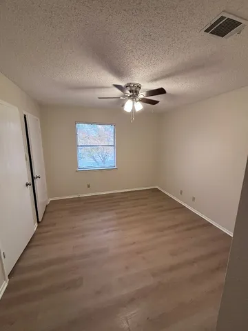 an empty room with wooden floor fan and windows
