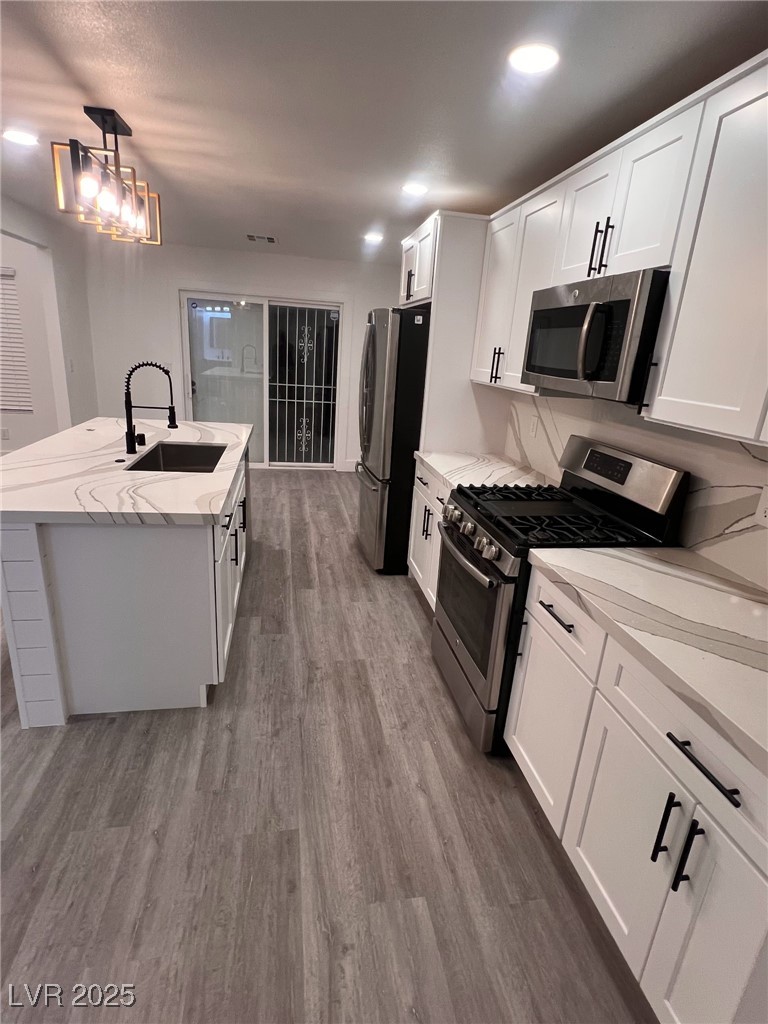 3686 Lincoln Road Las Vegas, NV 89115 - Photo 22 of 26 Kitchen featuring dark wood-style flooring, an island with sink, white cabinetry, stainless steel appliances, and a sink