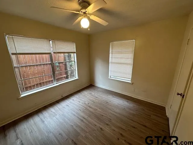 a view of an empty room with wooden floor and fan