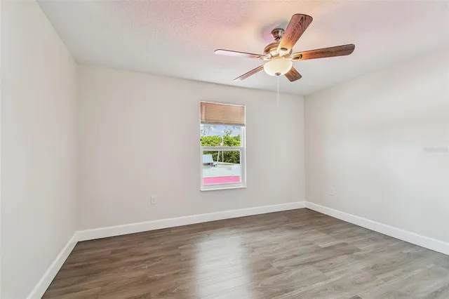 an empty room with wooden floor window and ceiling fan