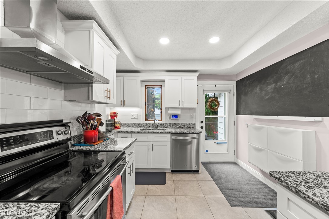 14420 Superior Road Cleveland, OH 44118 - Photo 15 of 44 Kitchen with stainless steel appliances, wall chimney exhaust hood, a sink, white cabinets, and light stone countertops