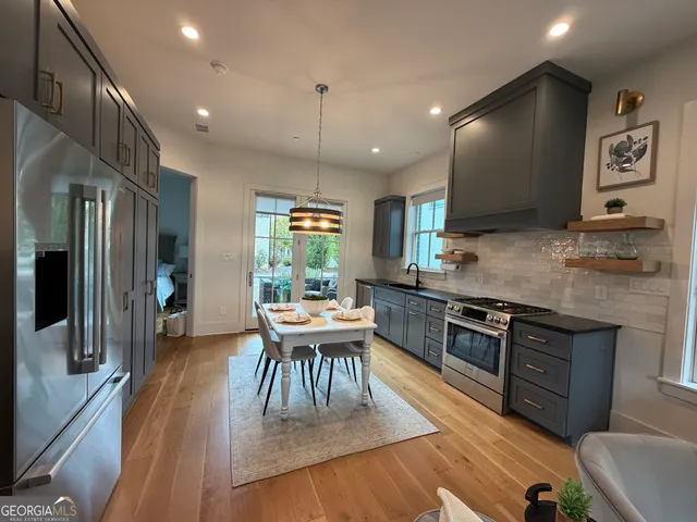 a kitchen with stainless steel appliances granite countertop a stove top oven a sink a dining table and chairs with wooden floor