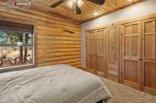 111 Blue Spruce Road Divide, CO 80814 - Photo 30 of 46 Bedroom with log walls, a closet, wood ceiling, carpet, and a ceiling fan