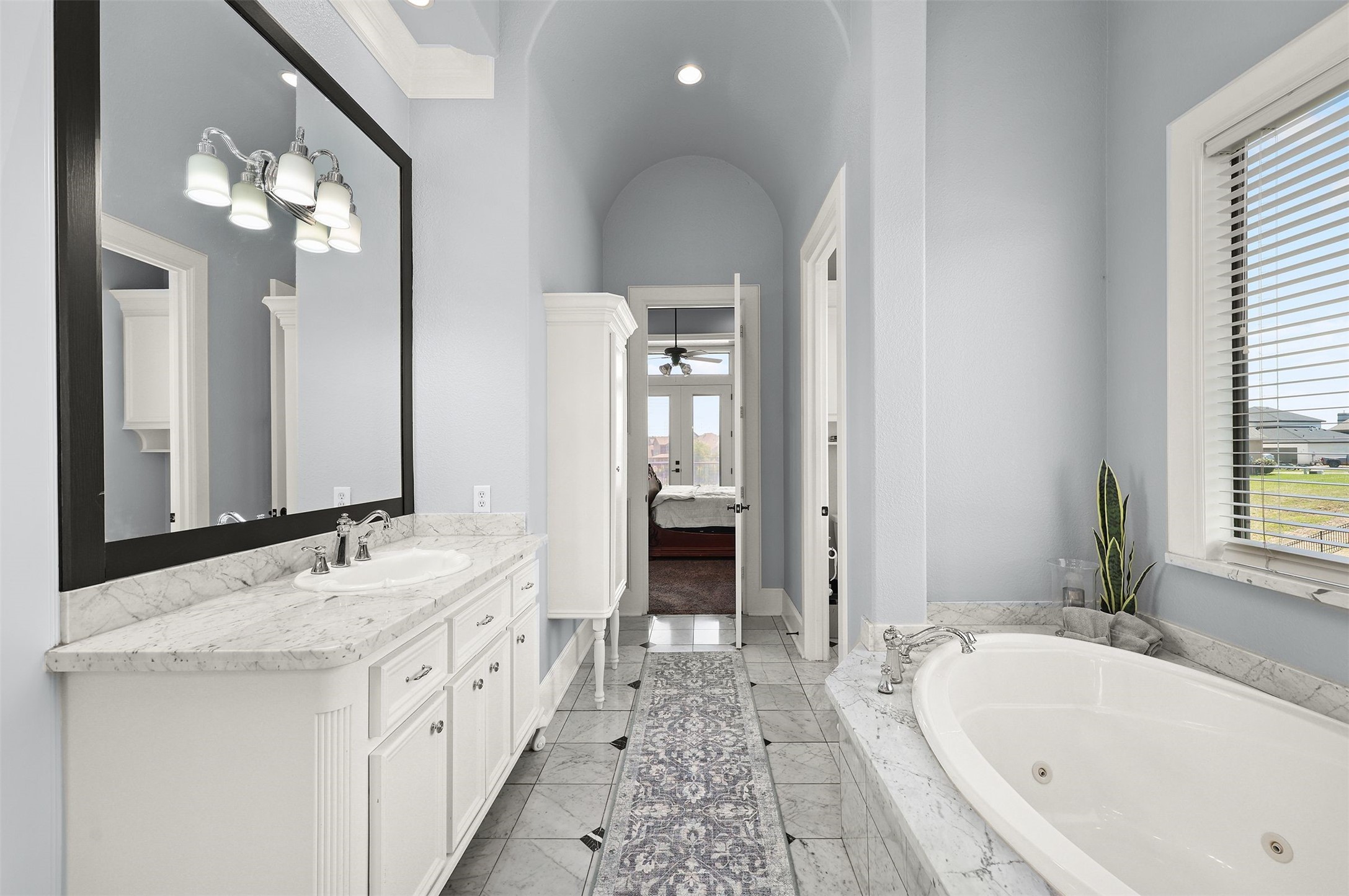 10896 Decatur Street Willis, TX 77318 - Photo 35 of 50 This elegant bathroom boasts a spacious layout with a large vanity featuring dual sinks, marble countertops, and a luxurious soaking tub, all enhanced by natural light, serene light blue walls, and modern fixtures for a tranquil retreat.