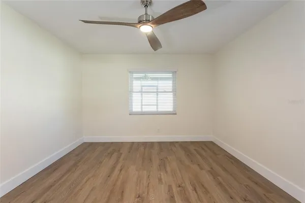 an empty room with wooden floor ceiling fan and window