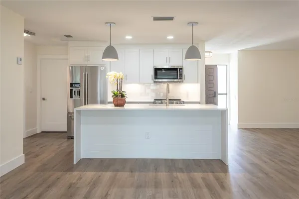 a large kitchen with kitchen island a refrigerator a sink dishwasher a oven with white cabinets and wooden floor