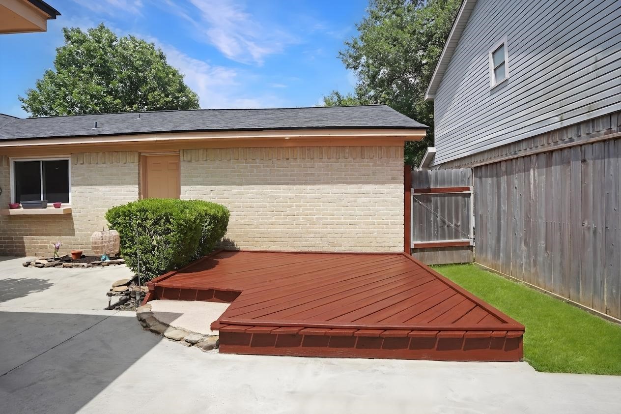 17119 Mellow Ridge Drive Spring, TX 77379 - Photo 25 of 32 This photo shows a cozy backyard area featuring a small wooden deck with a fresh reddish-brown stain, adjacent to a light brick exterior wall. There's a well-maintained hedge and a wooden fence providing privacy, along with a small patch of grass. Perfect for outdoor relaxation.