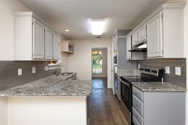 a kitchen with granite countertop a sink a stove top oven a counter space and cabinets