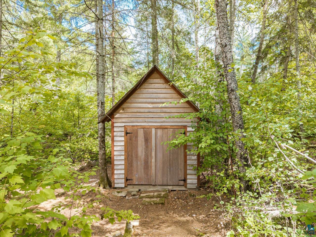 10401 Gunsten Lake Road Isabella, MN 55607 - Photo 50 of 91 Wood-sided shed with a peaked roof, double wooden doors with black hinges, surrounded by mature trees and lush foliage