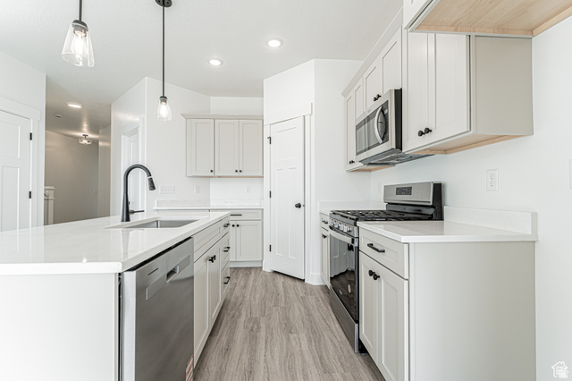 4774 Alder Drive Mapleton, UT 84664 - Photo 4 of 27 Kitchen featuring stainless steel appliances, light wood-type flooring, an island with sink, pendant lighting, and light stone countertops