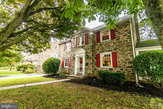 a view of a brick house with a yard plants and large tree