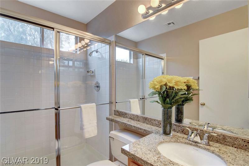 2647 Ridgewater Circle Henderson, NV 89074 - Photo 14 of 26 Polished granite countertops complement a bright vanity mirror and a glass-enclosed walk-in shower.