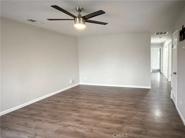 a view of an empty room with wooden floor and a ceiling fan