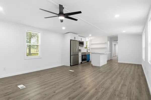 an empty room with wooden floor a ceiling fan and kitchen view