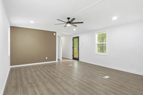 an empty room with wooden floor ceiling fan and windows
