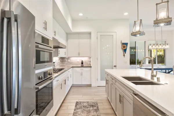 a kitchen with stainless steel appliances kitchen island granite countertop a stove a sink a refrigerator and white cabinets with wooden floor