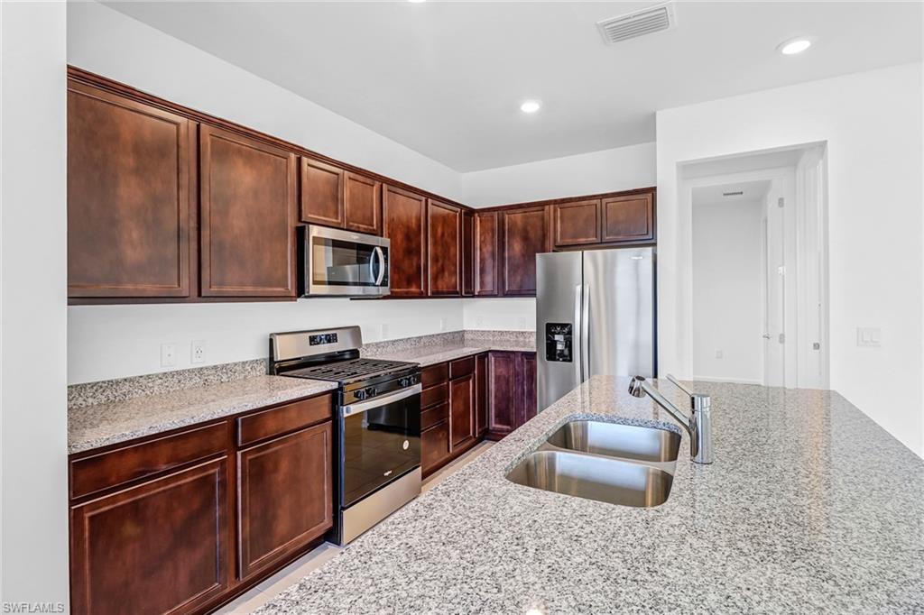 2167 Yellowfin Circle Naples, FL 34114 - Photo 9 of 36 a kitchen with granite countertop wooden cabinets a stove top oven a sink and dishwasher