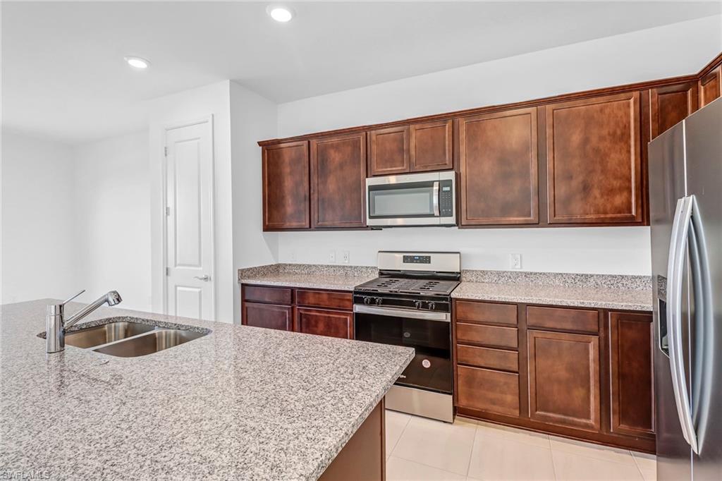 2167 Yellowfin Circle Naples, FL 34114 - Photo 10 of 36 a kitchen with stainless steel appliances granite countertop a stove a sink dishwasher and a microwave oven with wooden cabinets
